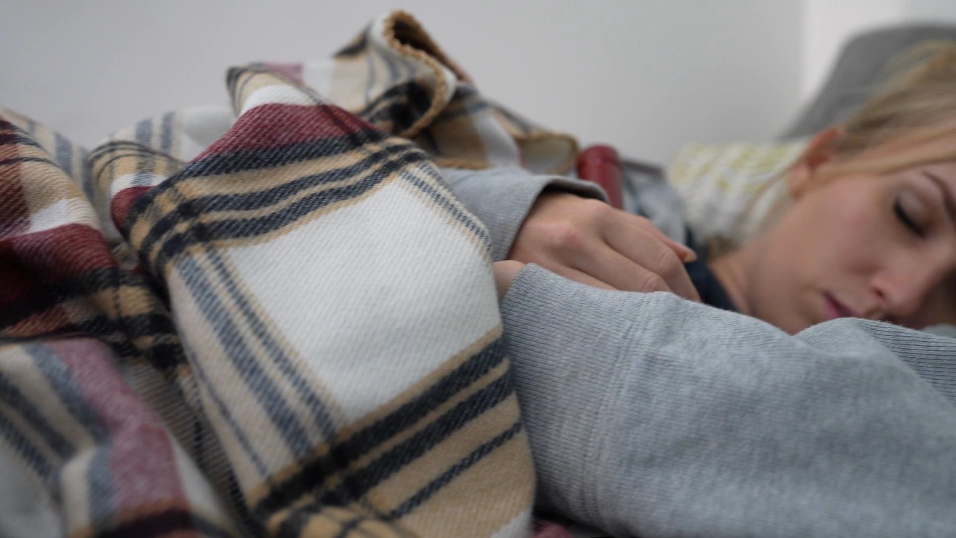 A couple enjoys time together on a couch before one individual falls asleep under a plaid blanket. The atmosphere is calm and comfortable.