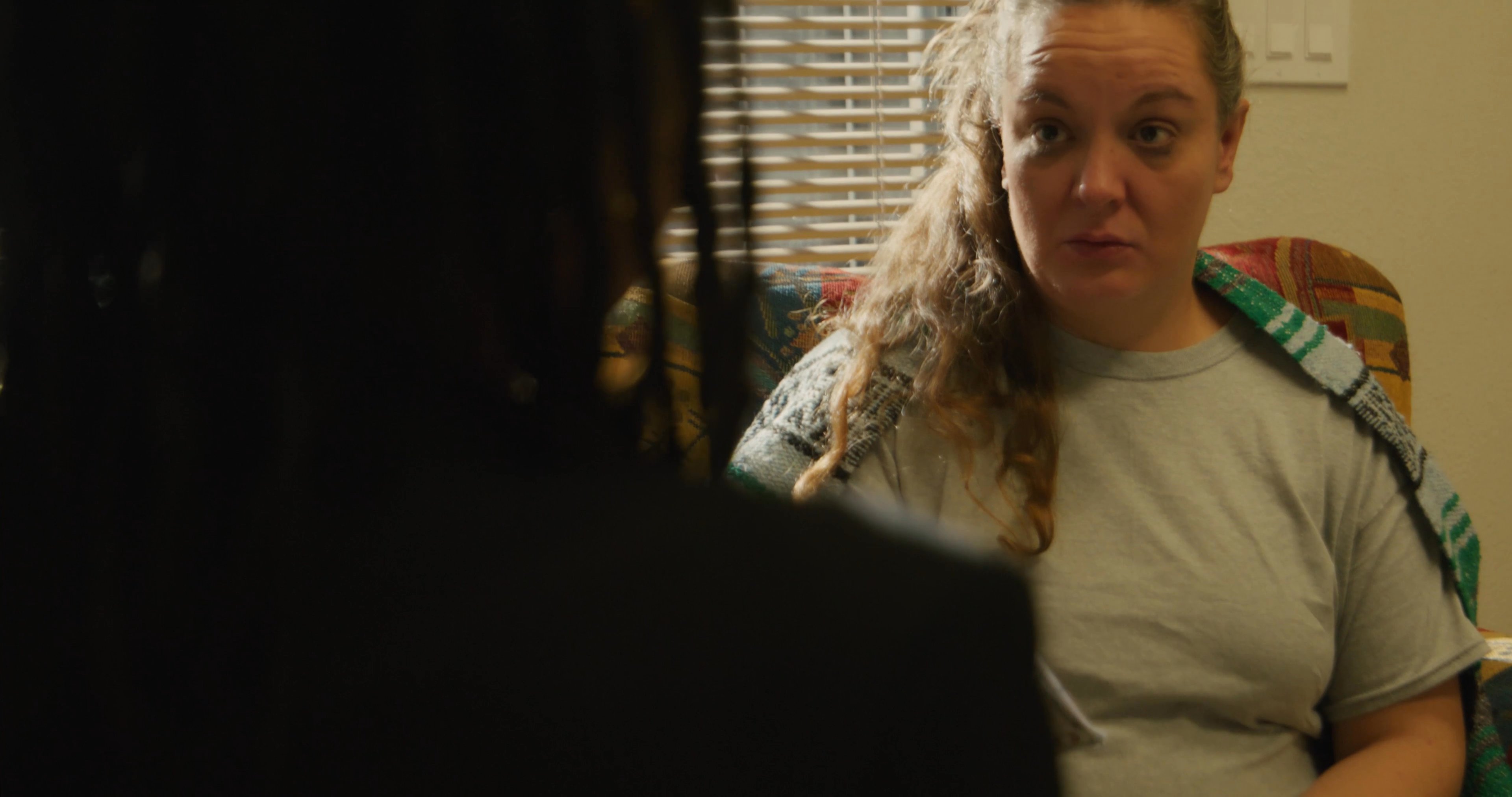A woman processing the loss of a loved one receives financial assistance during a counseling session. The contrast between a chaotic, memory-filled household and a structured support meeting highlights the complexity of her situation.