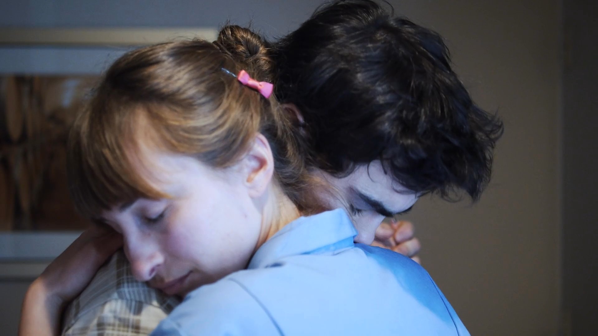 A man and a woman share an intimate, quiet moment while slowly dancing and embracing in a room.