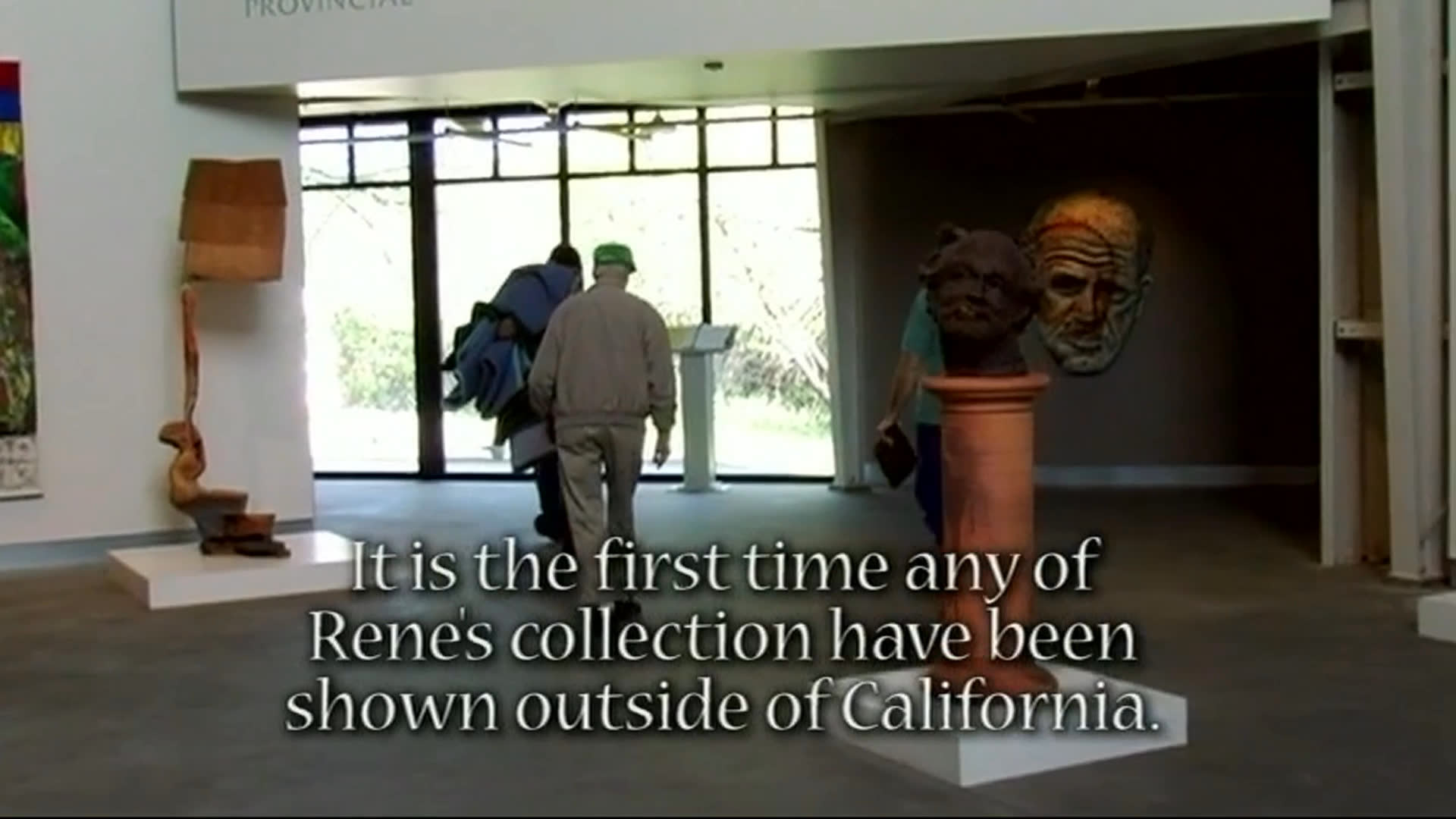 Men arrive with a truck and walk through a gallery displaying artworks and sculptures. An older man in a green cap speaks about the collection, which is being shown outside California for the first time.