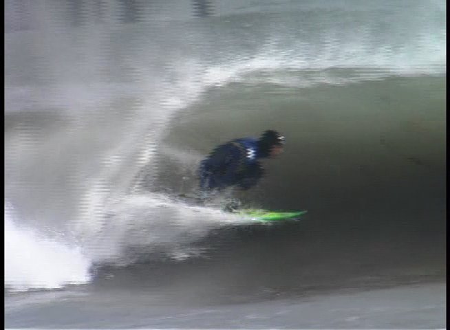 A skilled surfer maneuvers through challenging waves and barrels near a pier in an overcast coastal environment. The surfer executes various turns and rides the surf before being enveloped by breaking waves.