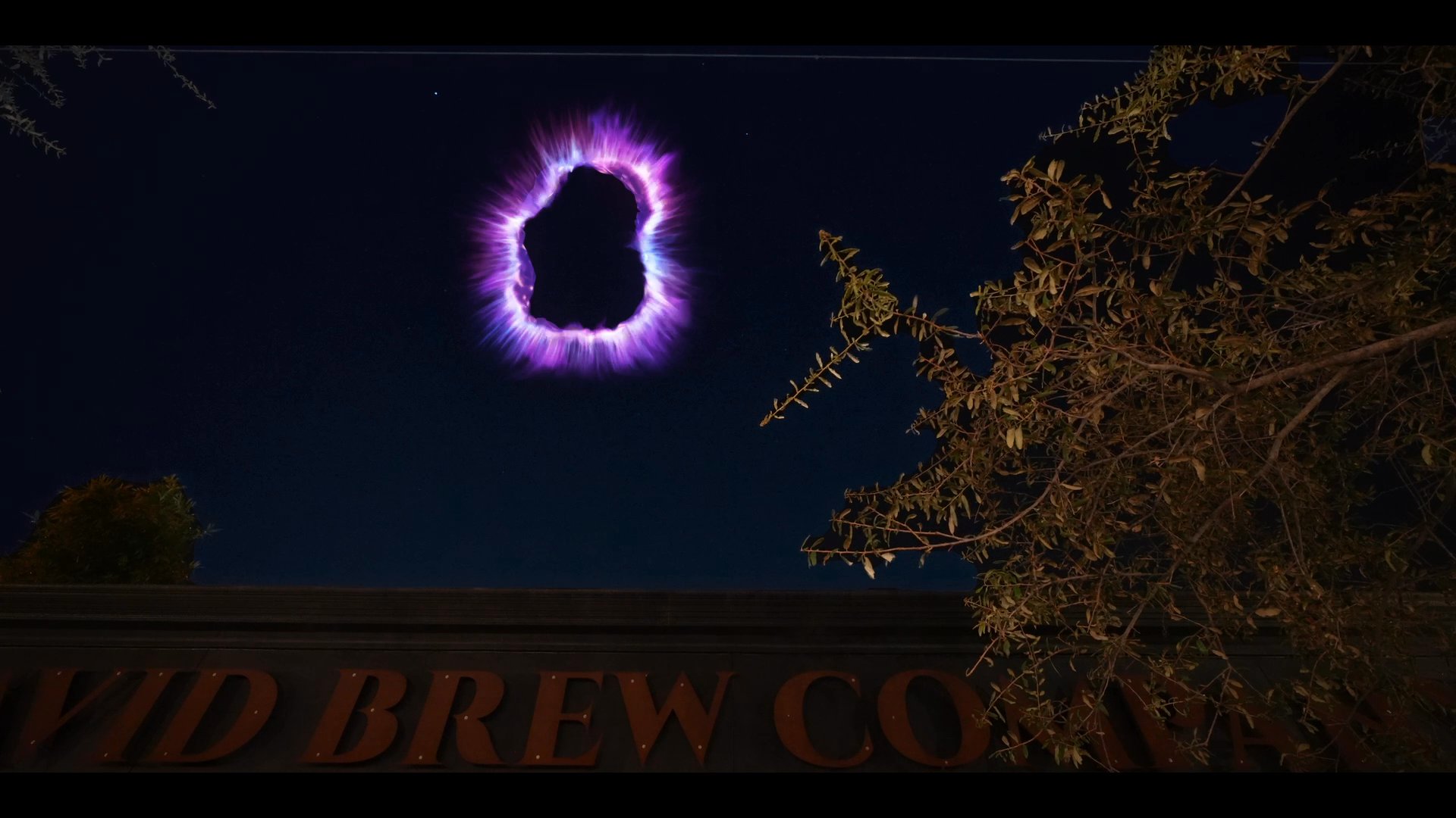 Three individuals perform a ritual around an ouija board, manifesting a glowing purple portal in the night sky above a building. The participants maintain focus as the mystical energy appears before returning their attention to the board.