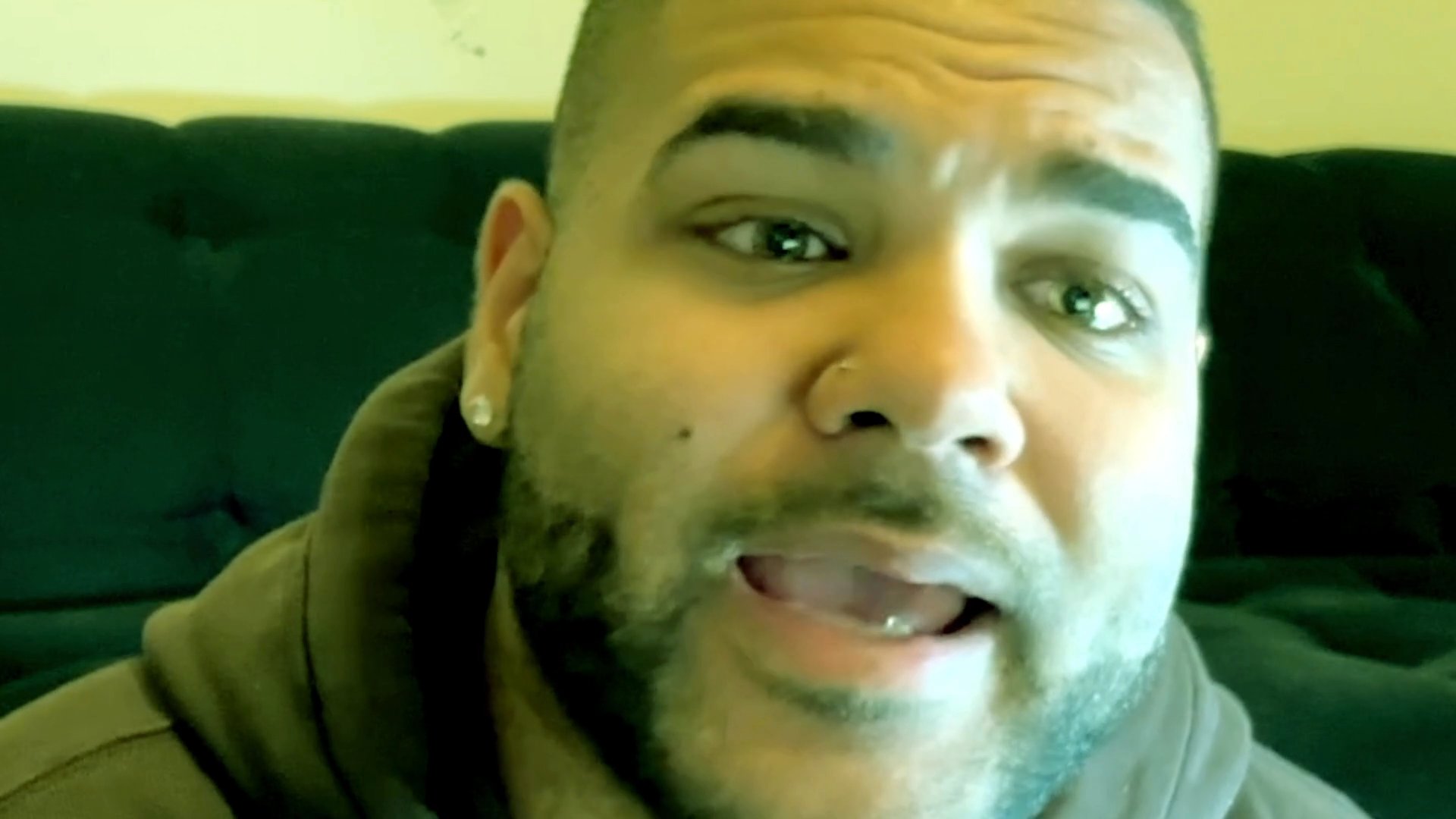 A man shares his perspective during a direct-to-camera monologue, engaging with the audience through expressive facial gestures and spoken communication.