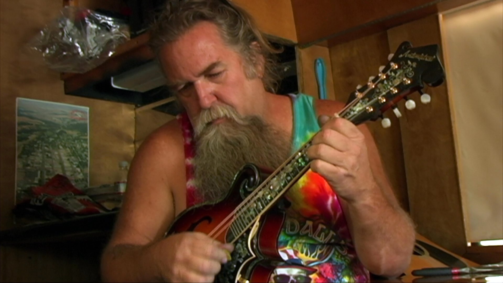 A bearded motorcyclist rides through a desert landscape, intercut with footage of the musician playing a mandolin and grazing bison in a field. The imagery captures a blend of adventurous travel, musical performance, and natural scenery.
