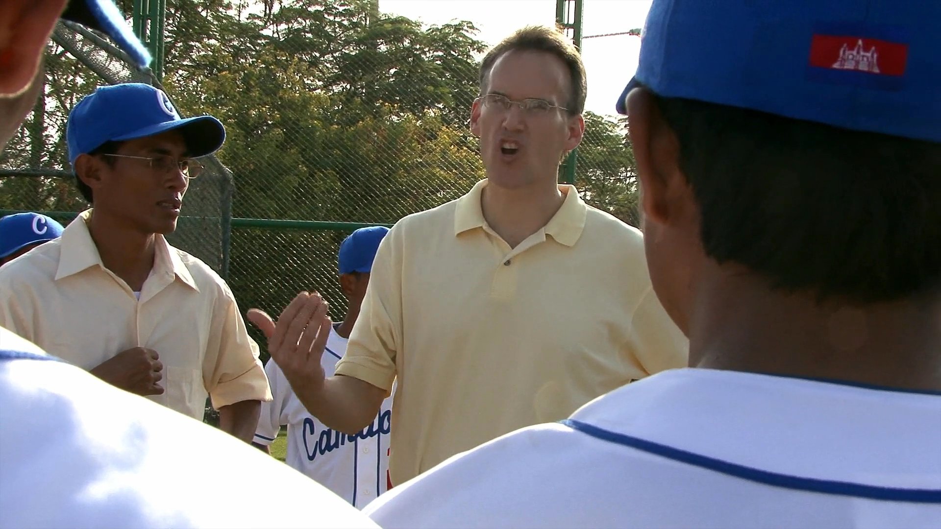 An instructor provides guidance and feedback to a youth baseball team during a practice session on an outdoor field. The coach gestures as he speaks to the players, fostering a focused and communicative learning environment.