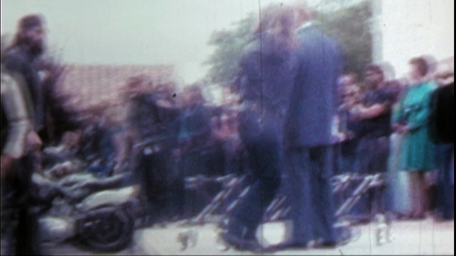 Mourners gather at a funeral service to pay respects as a casket is loaded into a hearse. The group of individuals, characterized by their motorcycle club attire, shares a solemn moment of consolation and tribute.