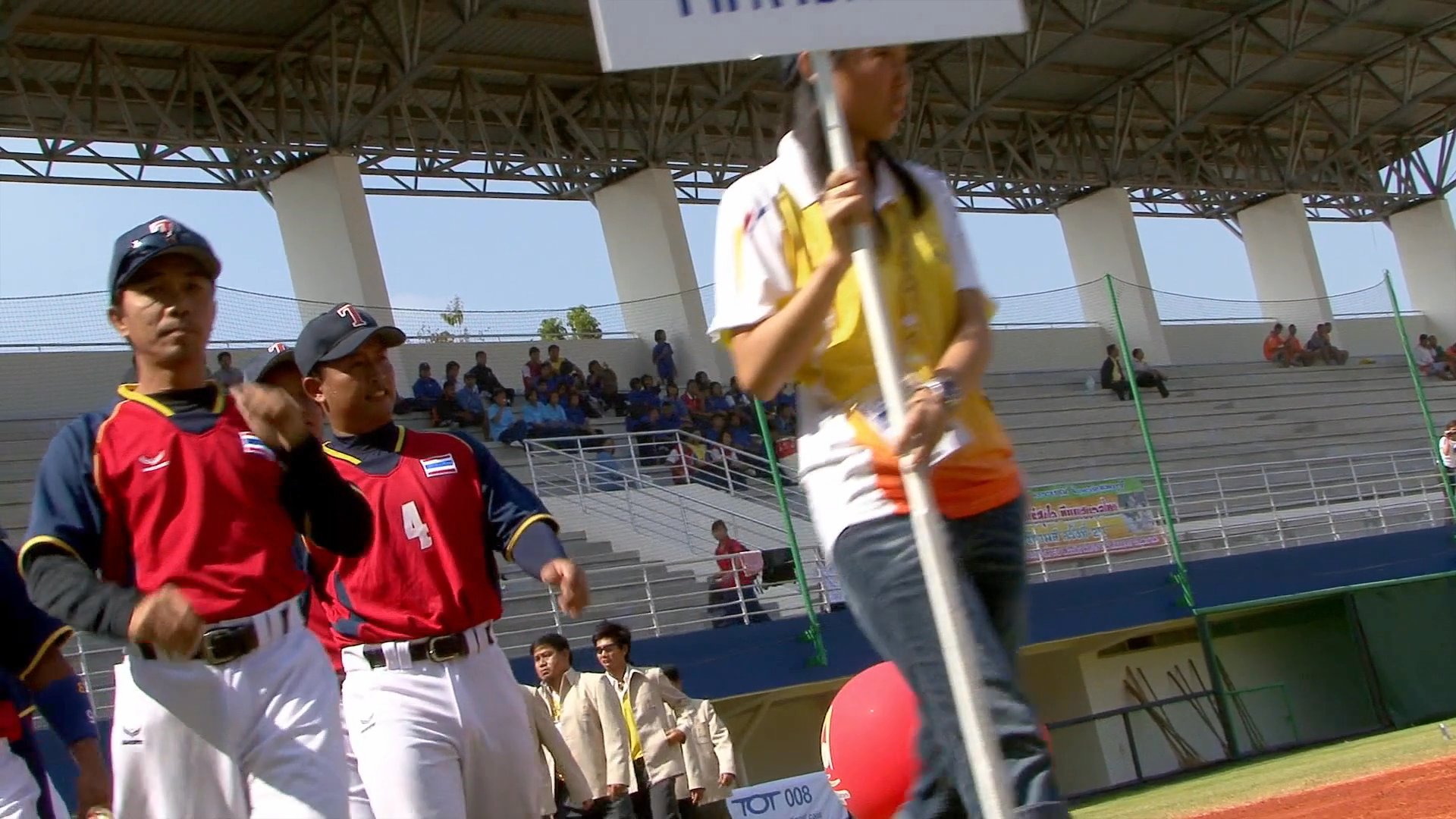 Athletes from various nations participate in an opening parade on a baseball field, representing their respective teams in an organized procession.