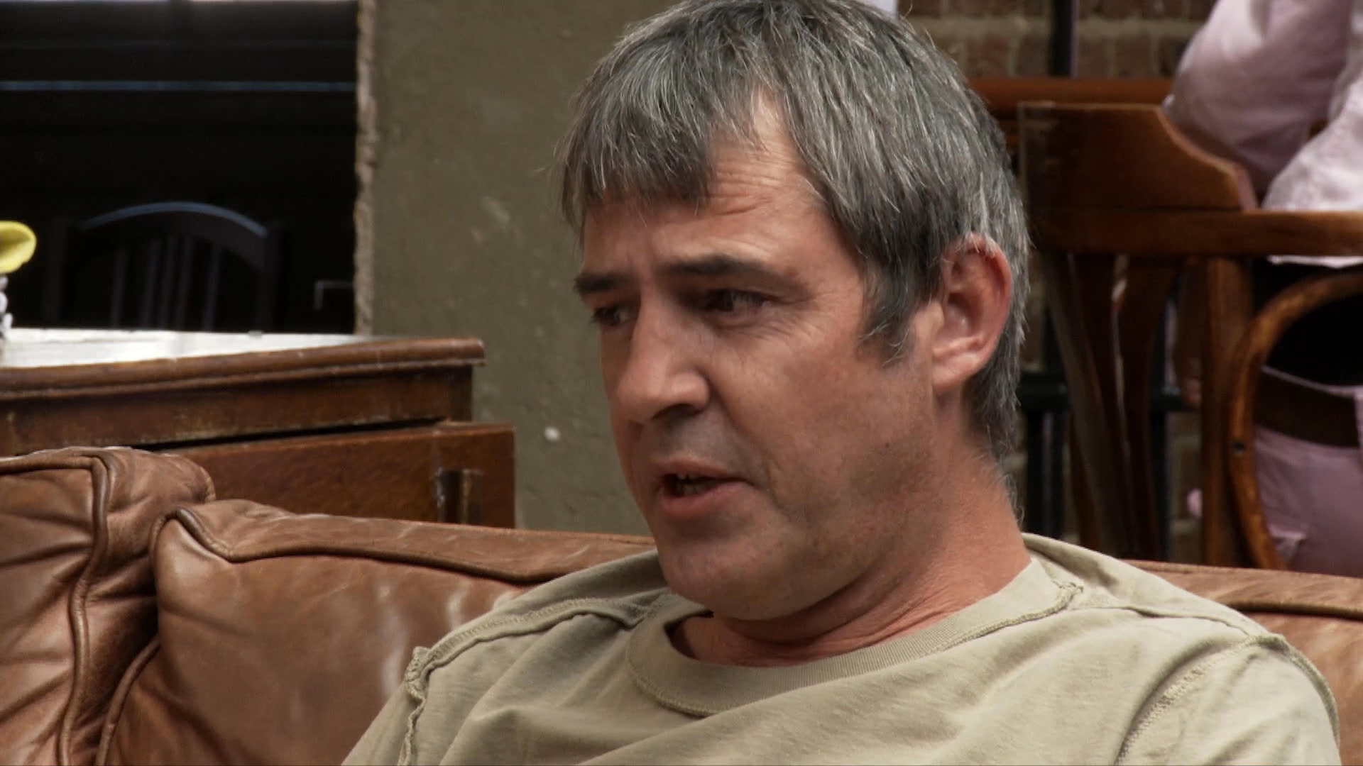 Two men engage in a serious discussion within a lounge setting before transitioning to an outdoor environment where they continue a conversation and work on sketches.