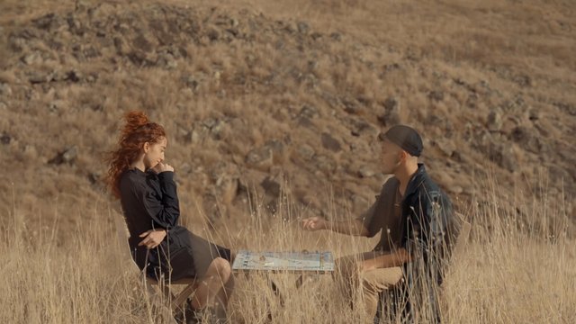 A couple playing a board game in the middle of a field of grass