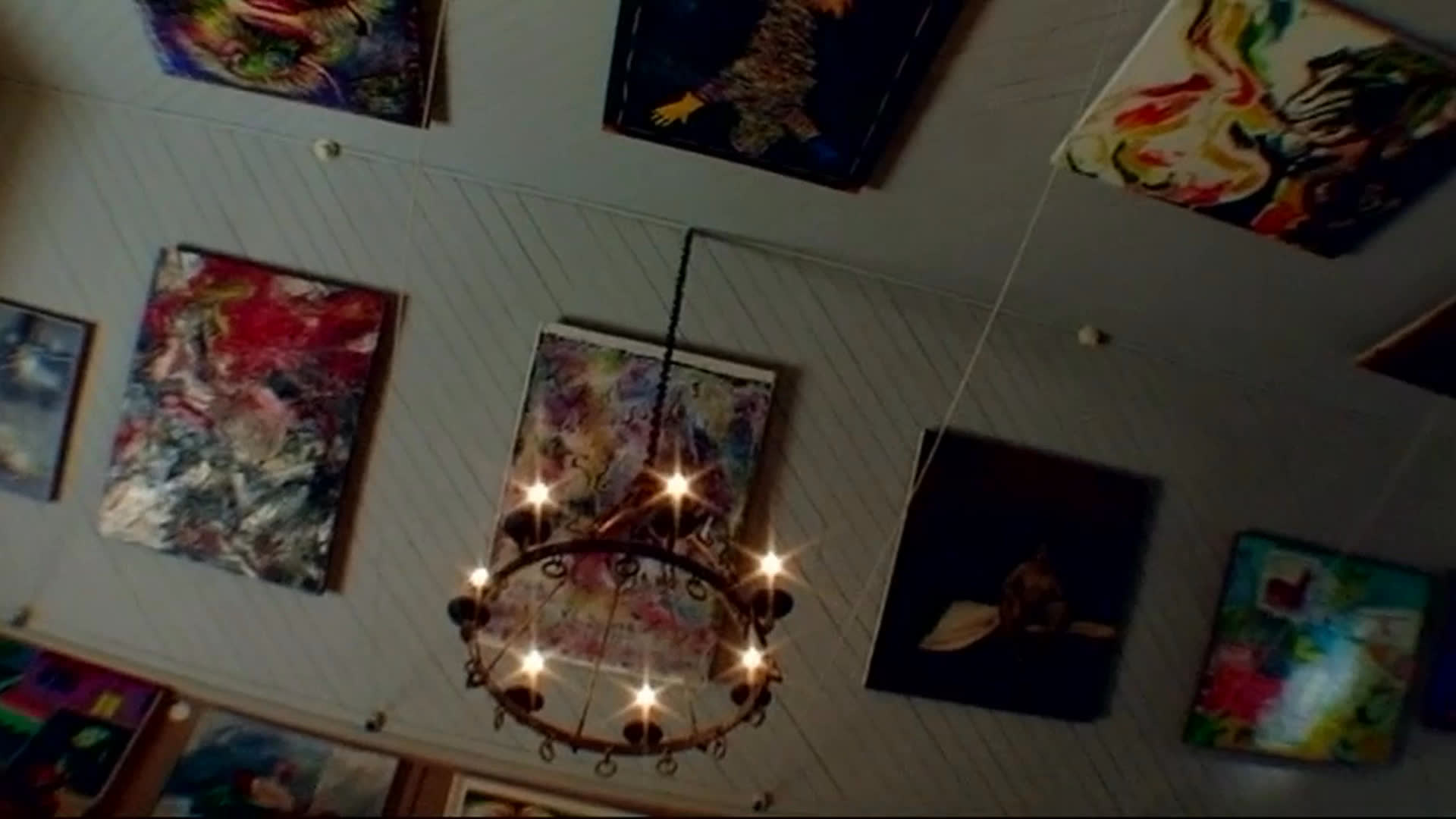 An art collector discusses the liveliness and depth of art and the pleasure of discovering work by artists who have never sold. Colorful contemporary paintings fill a gallery ceiling, while a large abstract sculpture stands outdoors beneath trees.