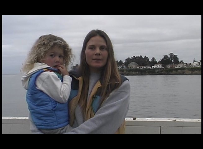 Individuals share reflections on local surf culture while positioned near a coastal pier. The footage highlights personal narratives and community history within a seaside setting.
