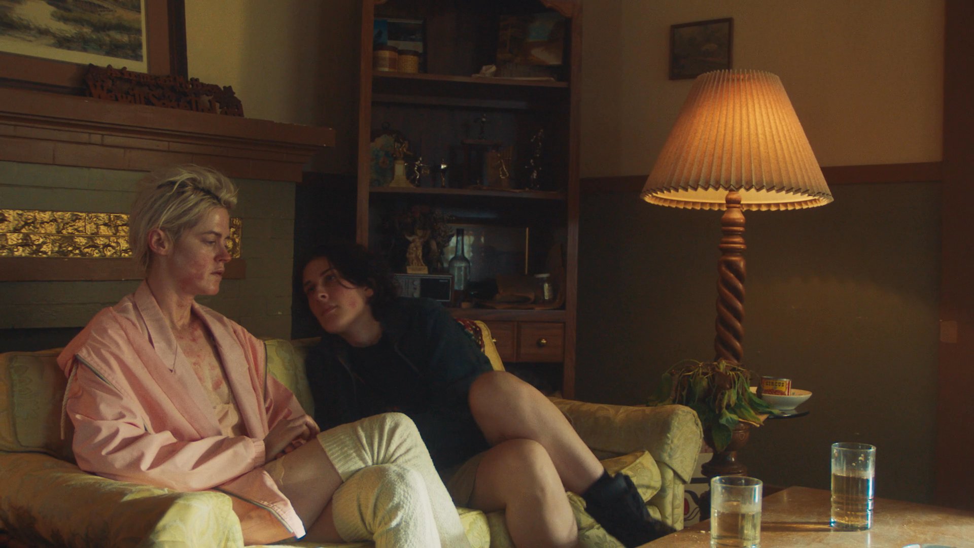 Two individuals engage in a quiet, intimate exchange while relaxing together on a sofa in a residential living room.
