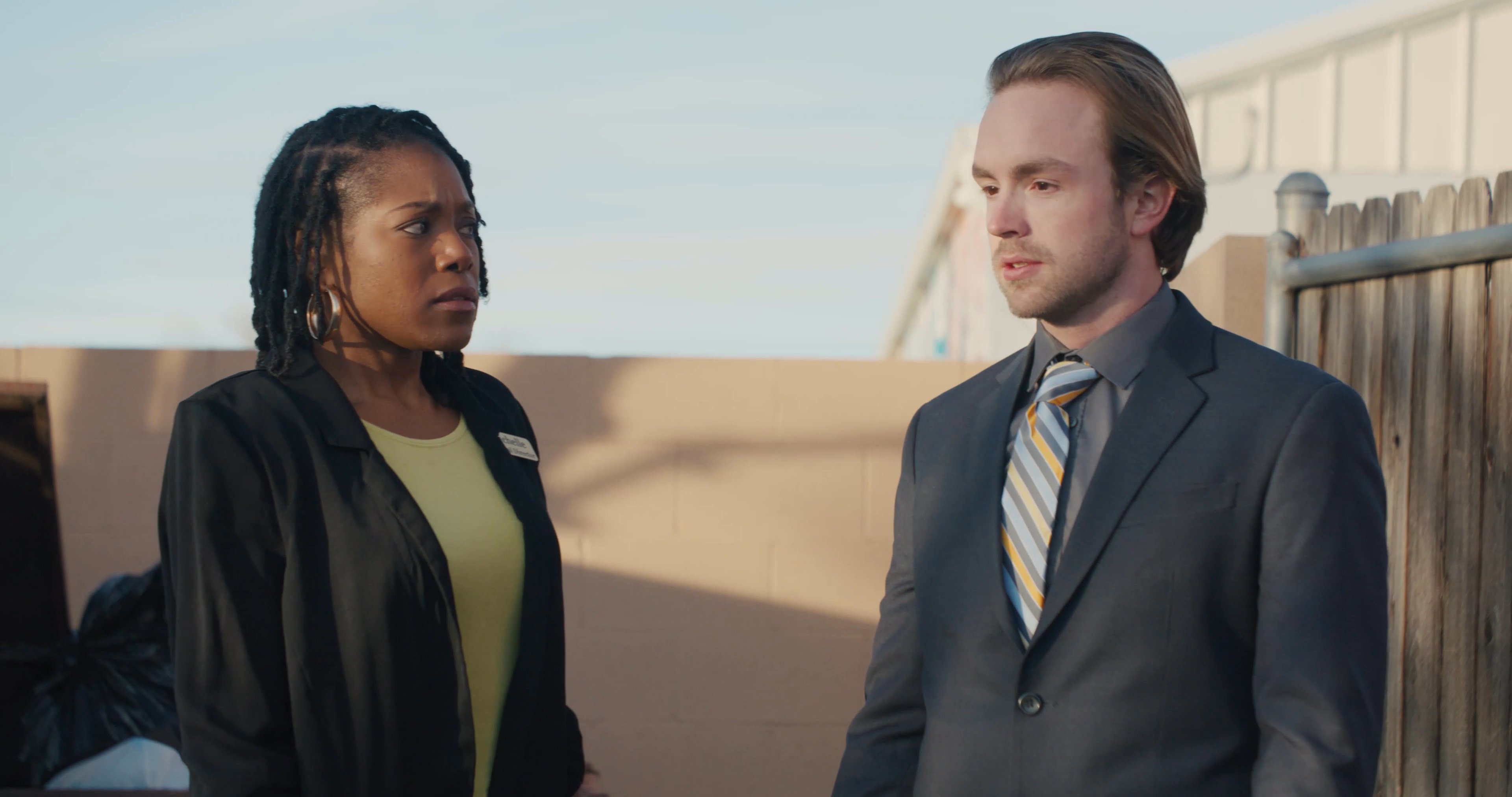 A couple embraces in an outdoor setting while two observers watch the interaction, eventually approaching the pair to engage in conversation.
