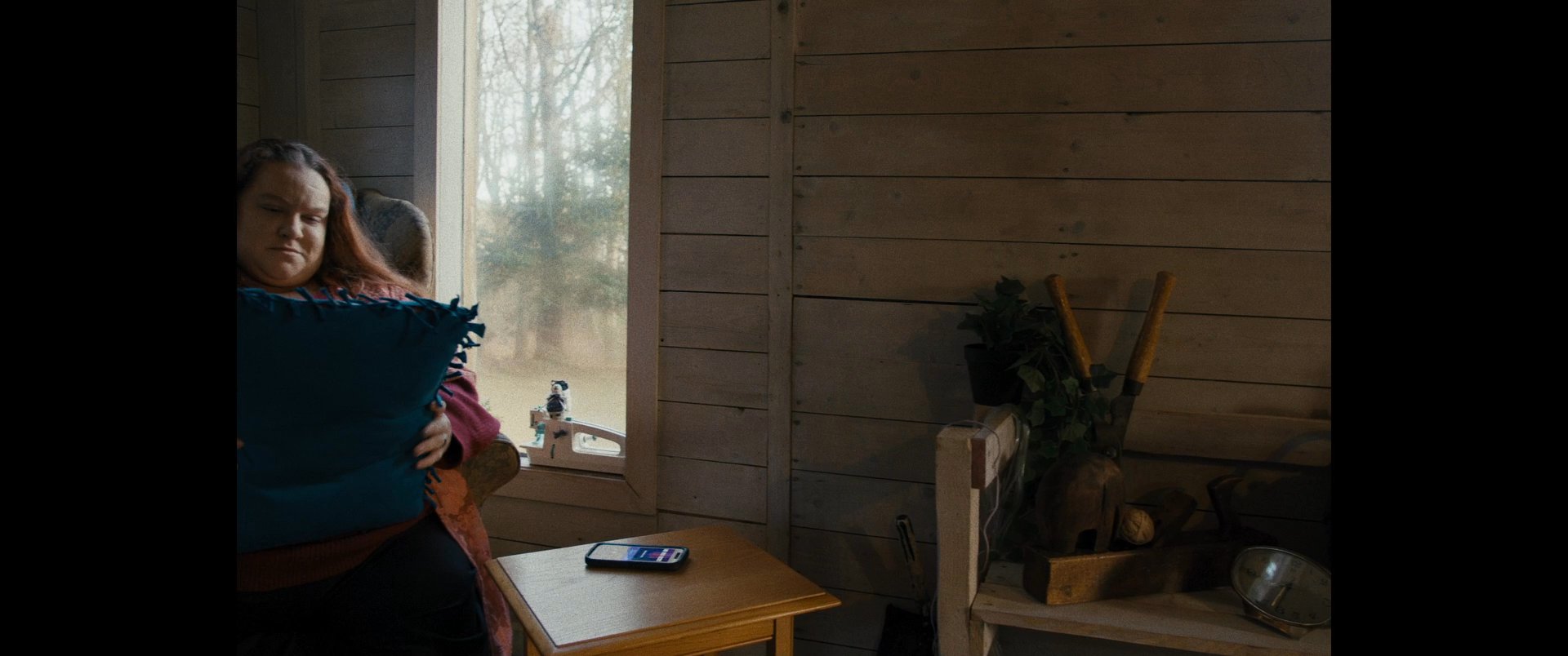 A woman sits in an armchair inside a cozy room, holding a blue pillow while relaxing. She eventually rises from the seat and exits the frame.