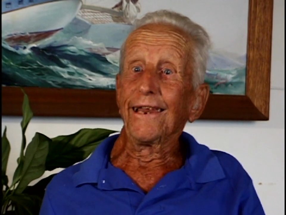 An elderly man shares personal stories and vivid memories about ocean waves, using expressive hand gestures to describe the scale and motion of the water.