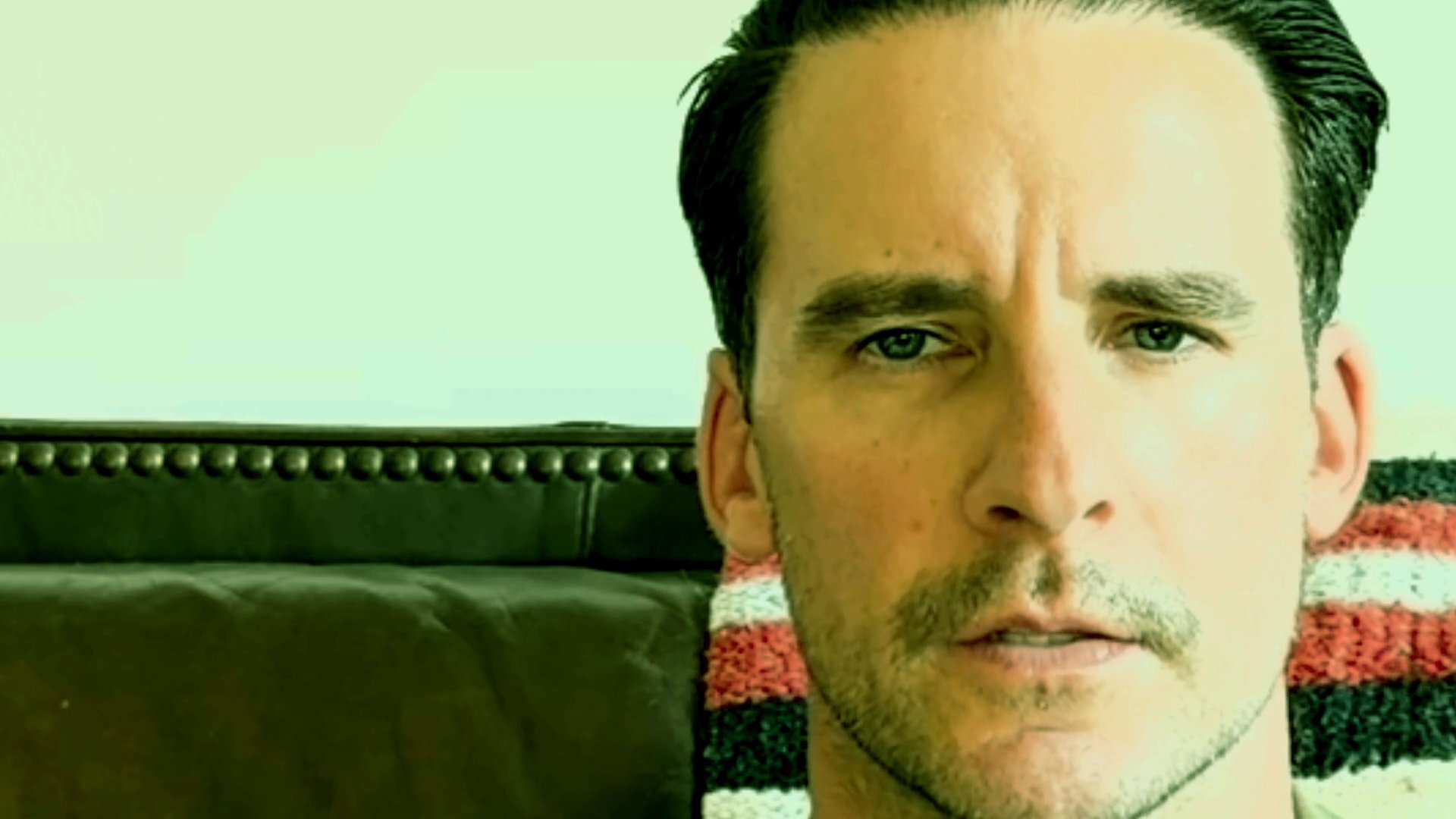 A man sits before the camera and shares a narrative, his facial expressions shifting as he speaks.