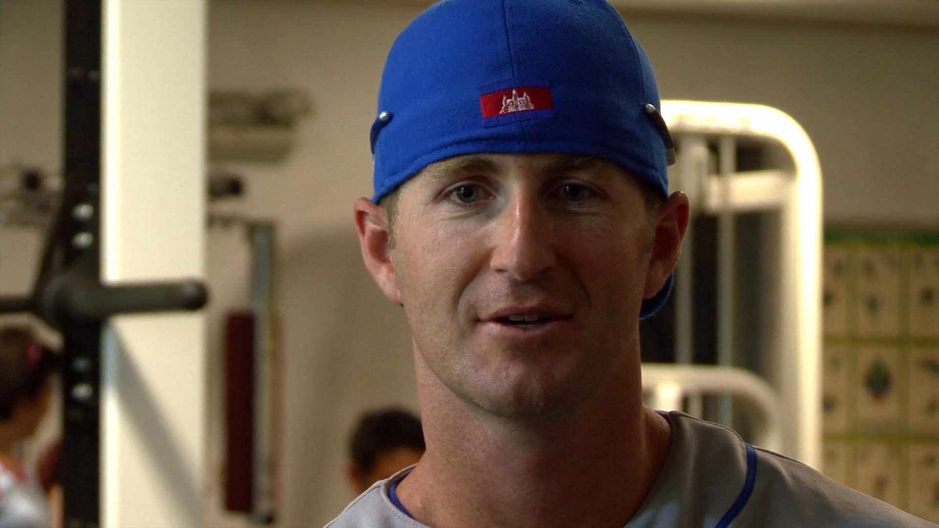 A professional athlete wearing a team cap discusses his training regimen and performance during an interview in a fitness gym.