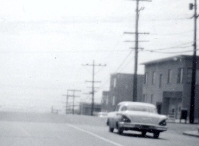 Aerial perspectives of a parking area transition into a low-angle view of a vintage car driving along an urban residential street.