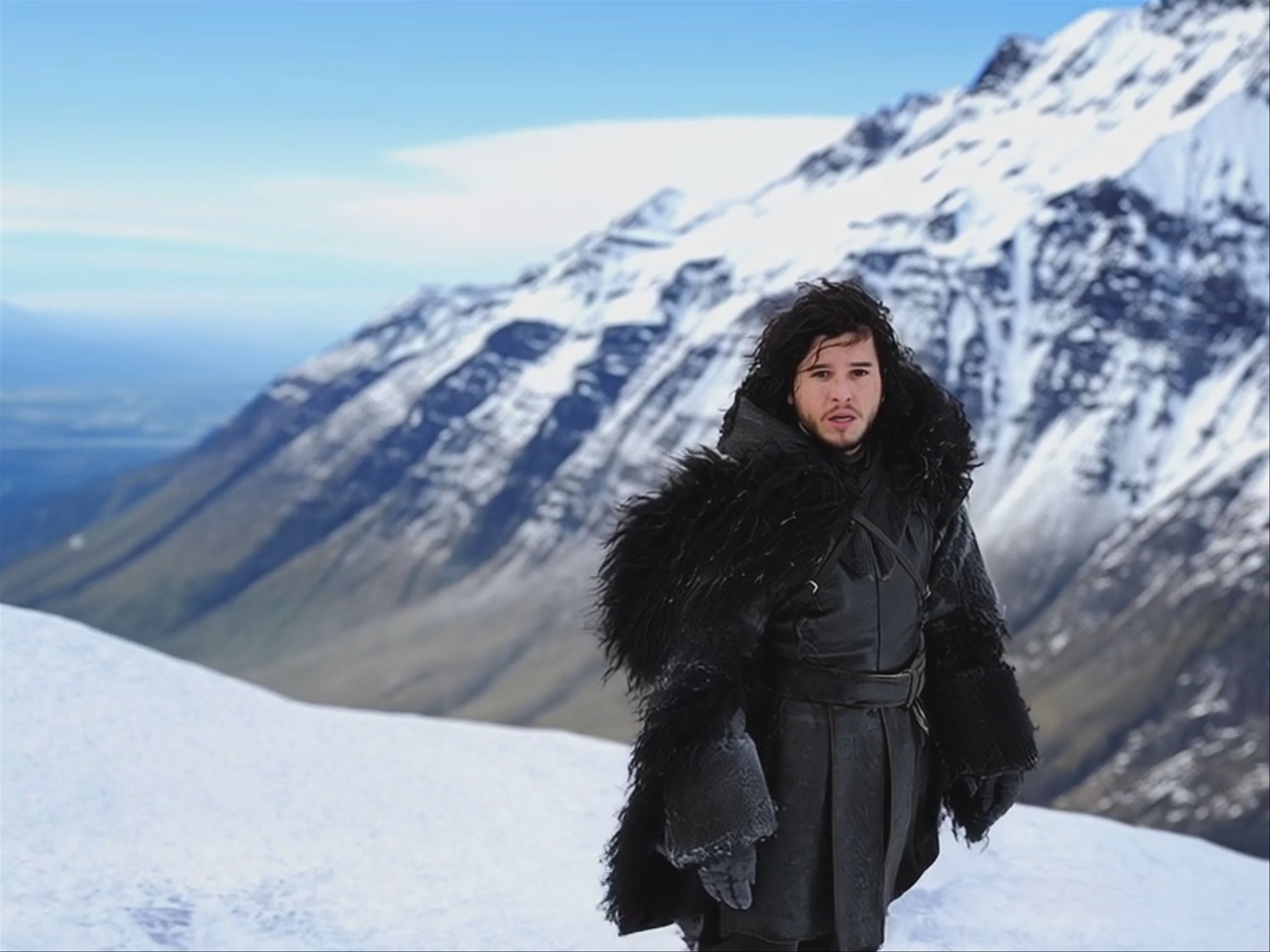 A close-up shot of a dark-haired man in a heavy black fur-trimmed cloak, standing against a backdrop of blurry, snow-covered mountains. Generated using MiniMax Hailuo 2.3 Fast Standard at a resolution of 1024x768, this video frame depicts a cinematic fantasy character with a serious expression.
