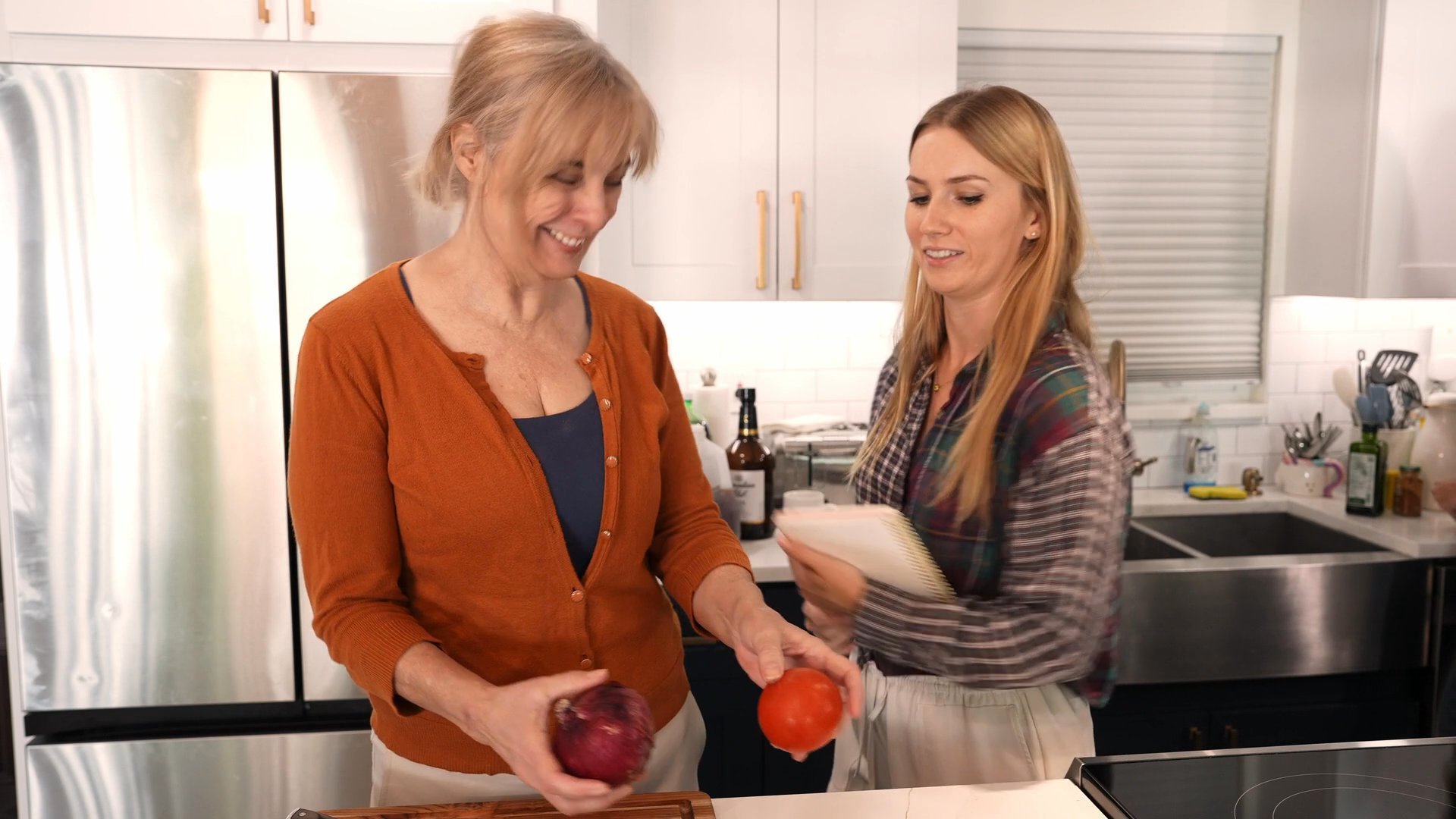 Two women prepare food in a kitchen while consulting a handwritten list, later transitioning to a discussion with a man in an adjacent room.