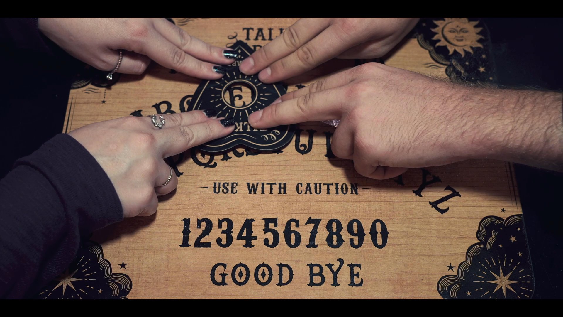 Three individuals participate in a tense seance, using a planchette to communicate with spirits on a ouija board by candlelight.