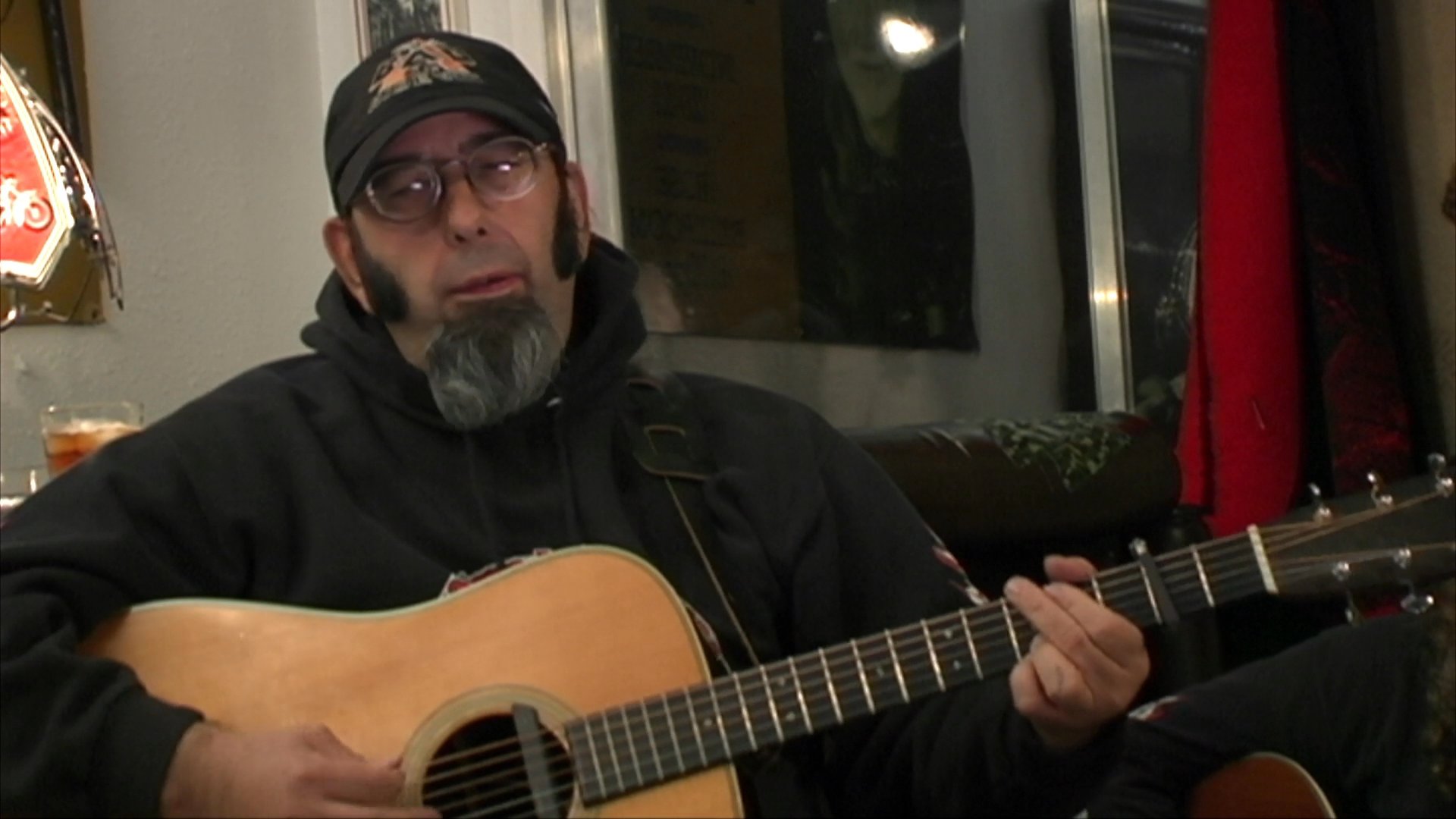 Two musicians perform a folk song in an indoor setting, with one playing acoustic guitar and the other accompanying on the violin.