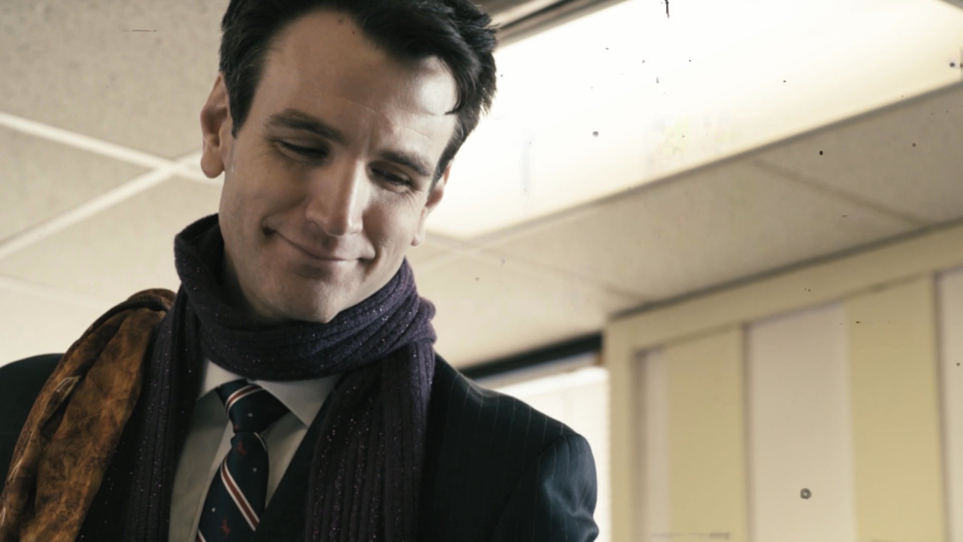 A man in a professional suit and scarf smiles warmly while visiting a casual restaurant setting with a child.