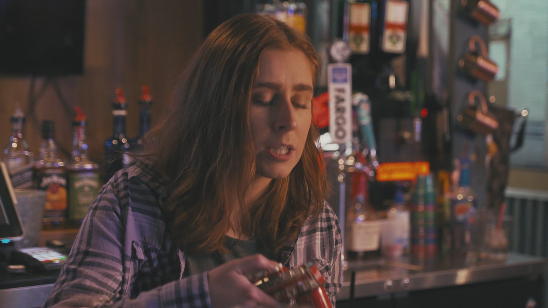 A man and a woman engage in conversation while seated at a bar counter. The scene transitions between their interaction and an exterior view of vehicles parked in a snow-covered environment.