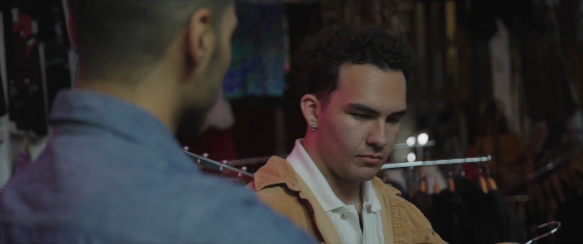 Two men browse through a clothing store together, examining items on hangers before the scene transitions to an outdoor view of a plaza.
