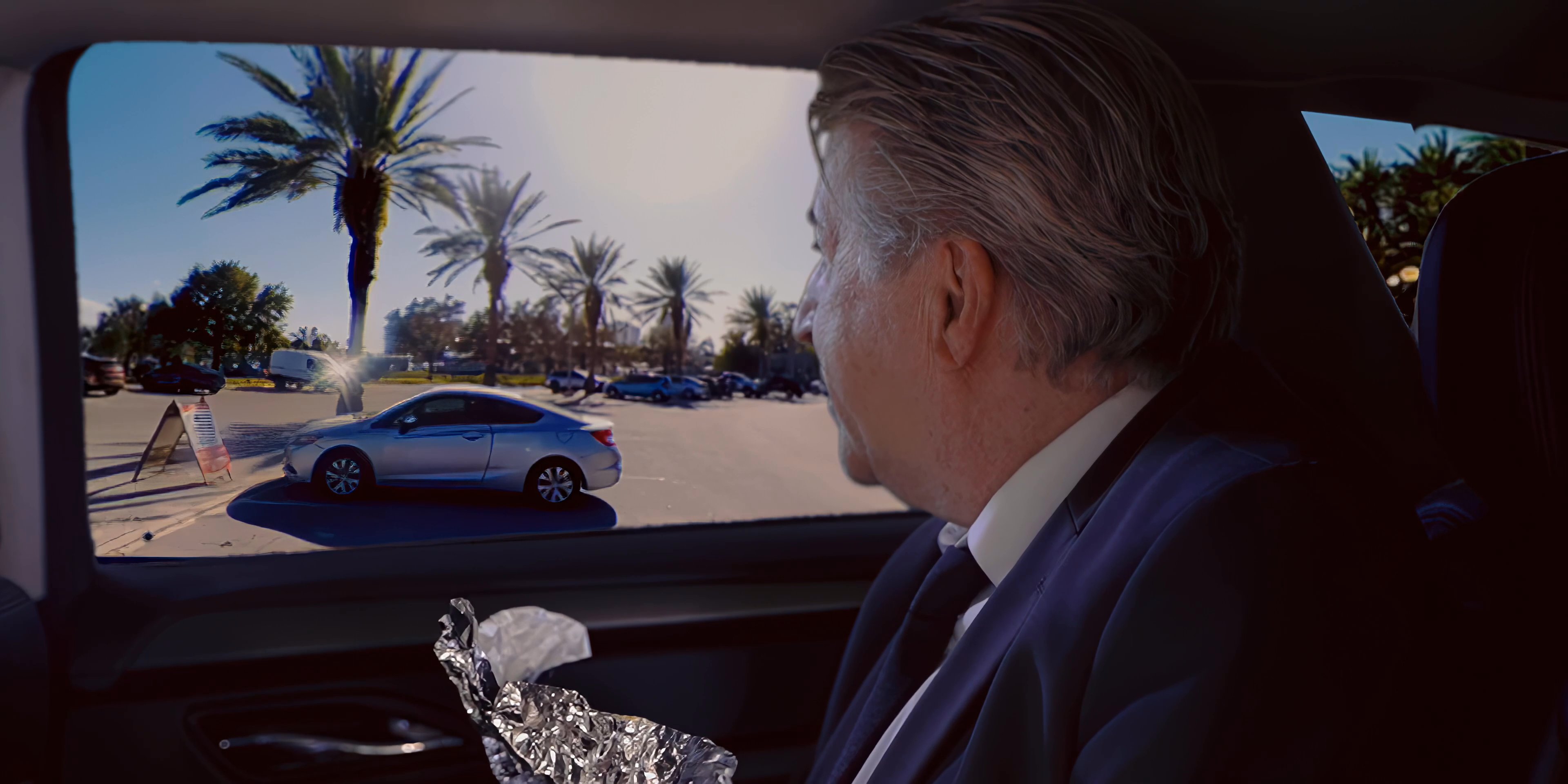 Two men sit inside a vehicle, engaging in a focused conversation while one person drives and the other observes the passing scenery.