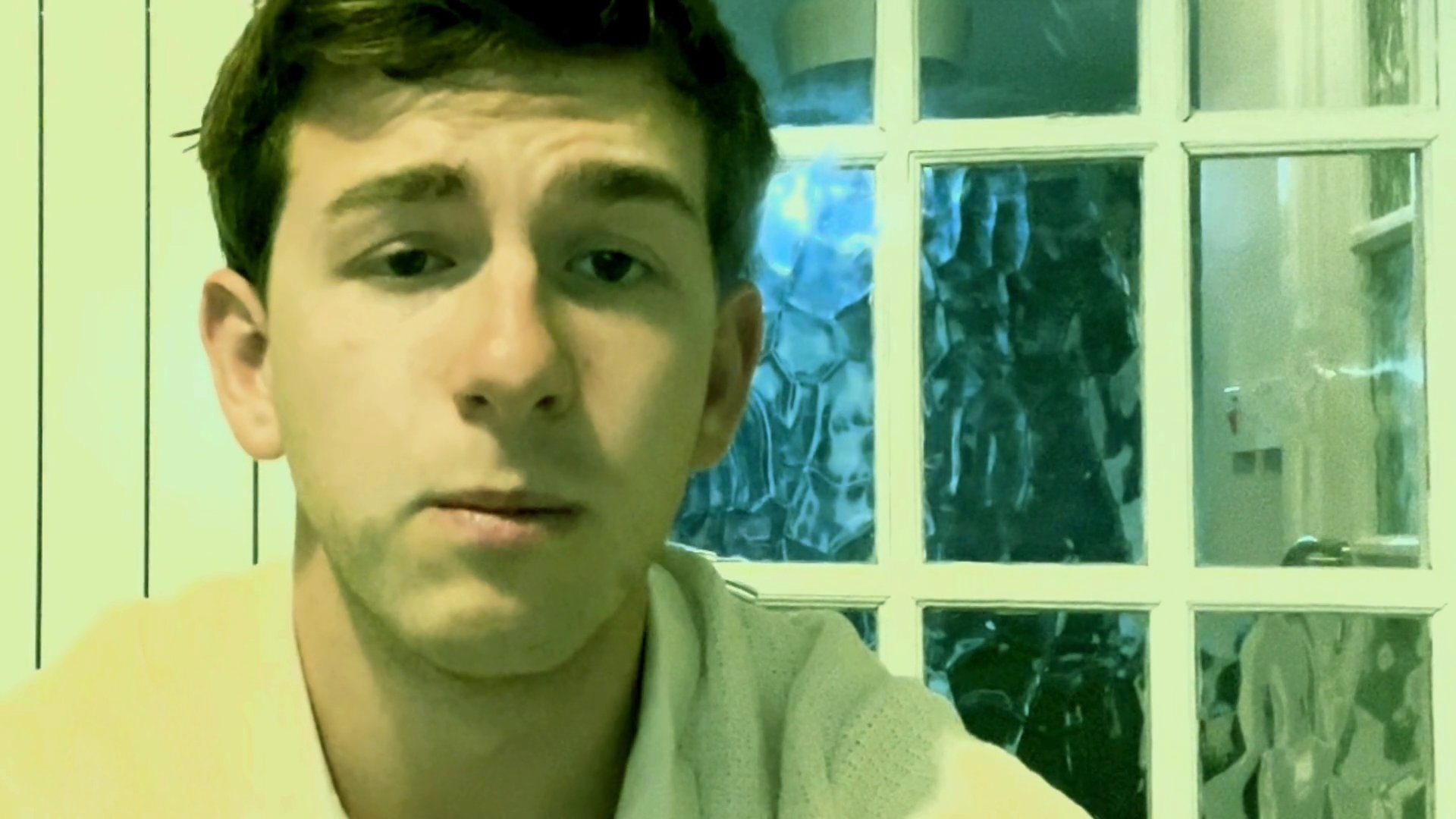 A young man sits indoors and speaks directly to the camera, sharing his thoughts in a conversational, vlog-style format.