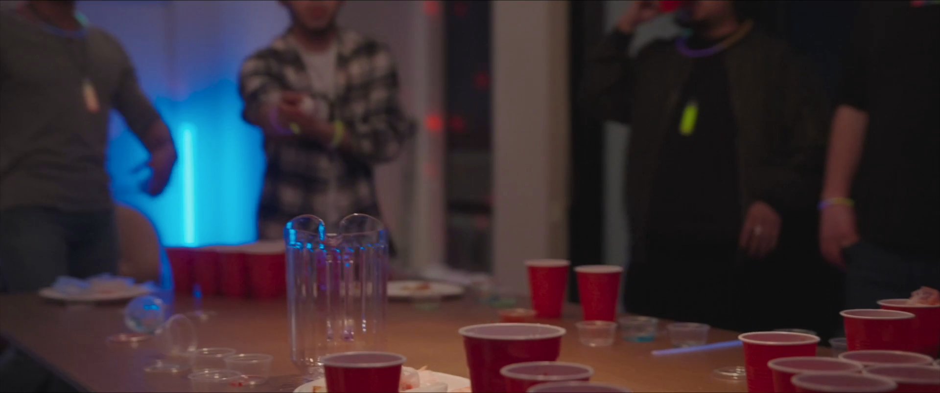 Young adults socialize and dance in a home setting at night, featuring a beer pong game and vibrant party atmosphere.