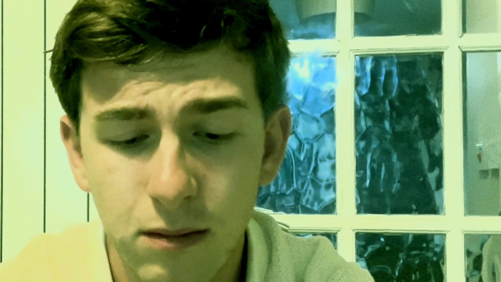 A young man speaks directly to the camera with expressive facial gestures while indoors. The sequence captures his focused engagement and natural speaking cadence.