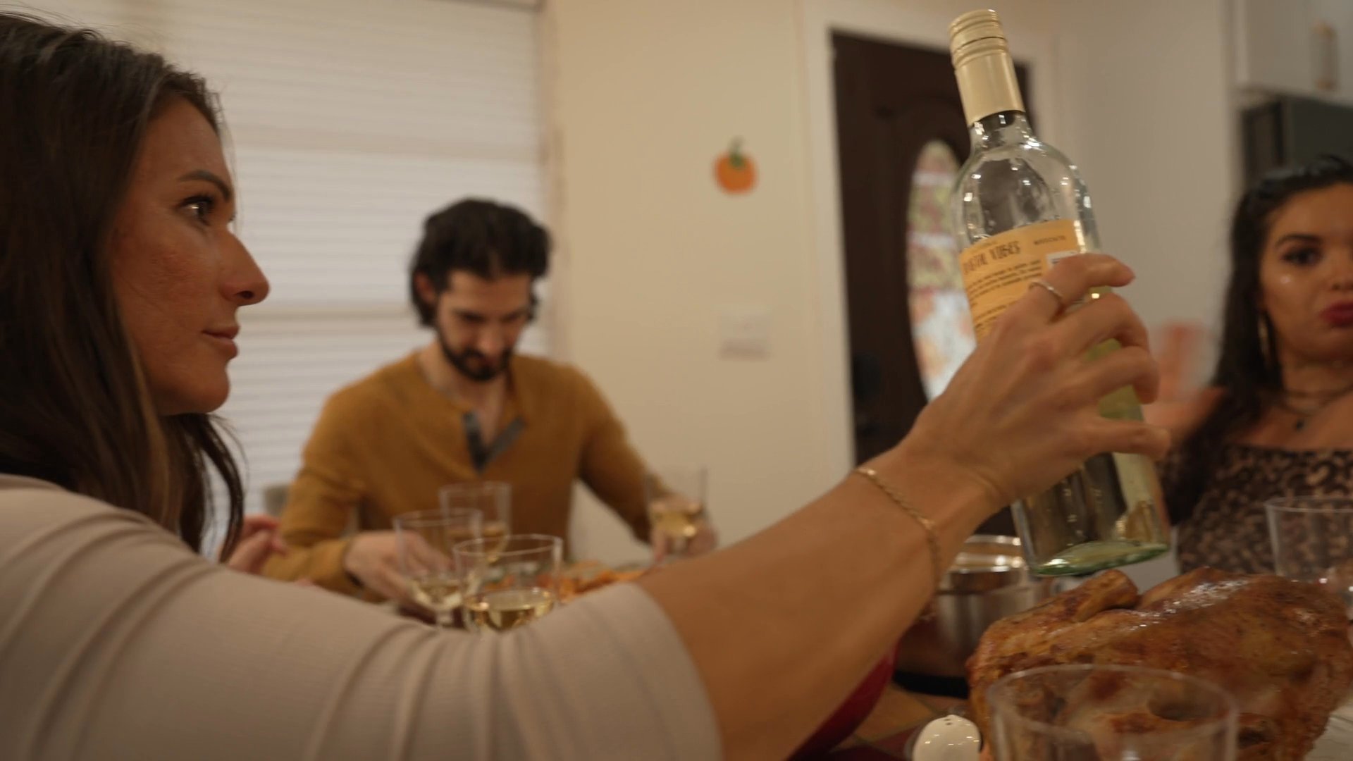 A group of friends shares a meal in a home setting, characterized by active social interaction and wine service.