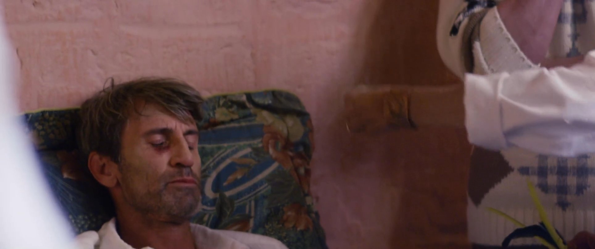 A practitioner performs a traditional cleansing ritual on a man resting in bed to facilitate his transformation and spiritual recovery. Observers watch quietly as the healer uses symbolic objects to clear energy and provide guidance.