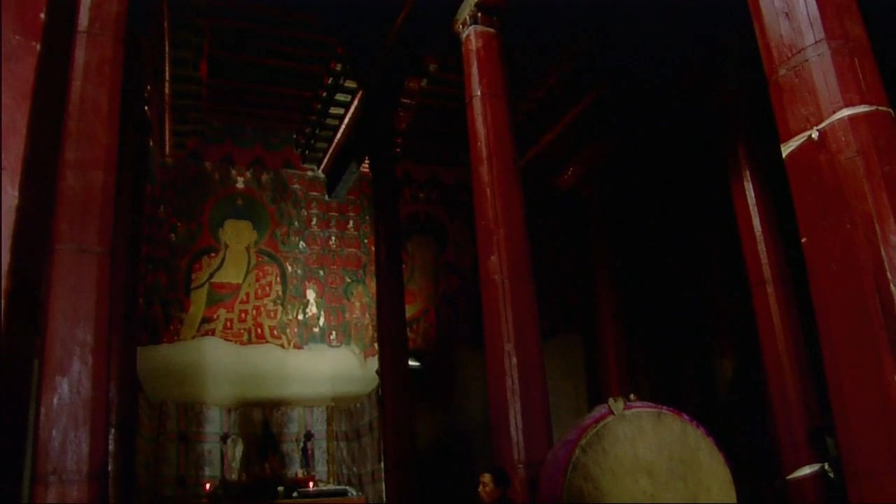 Buddhist monks perform a ceremonial ritual inside a dimly lit monastery, featuring rhythmic cymbal playing and meditative focus. The sequence transitions to an interview with Khempo Kungo Tenzing regarding the spiritual practice.