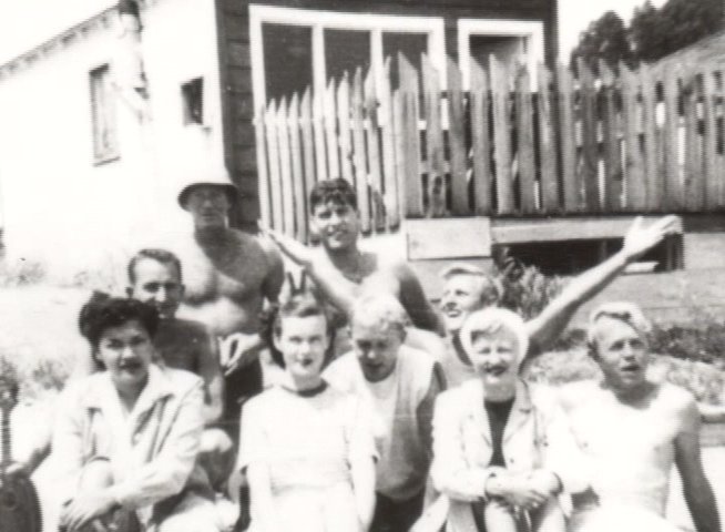 A group of veterans pose for a commemorative portrait in front of the historic Santa Cruz Surfing Club building. The scene captures a moment of community camaraderie preserved in a vintage black and white photograph.