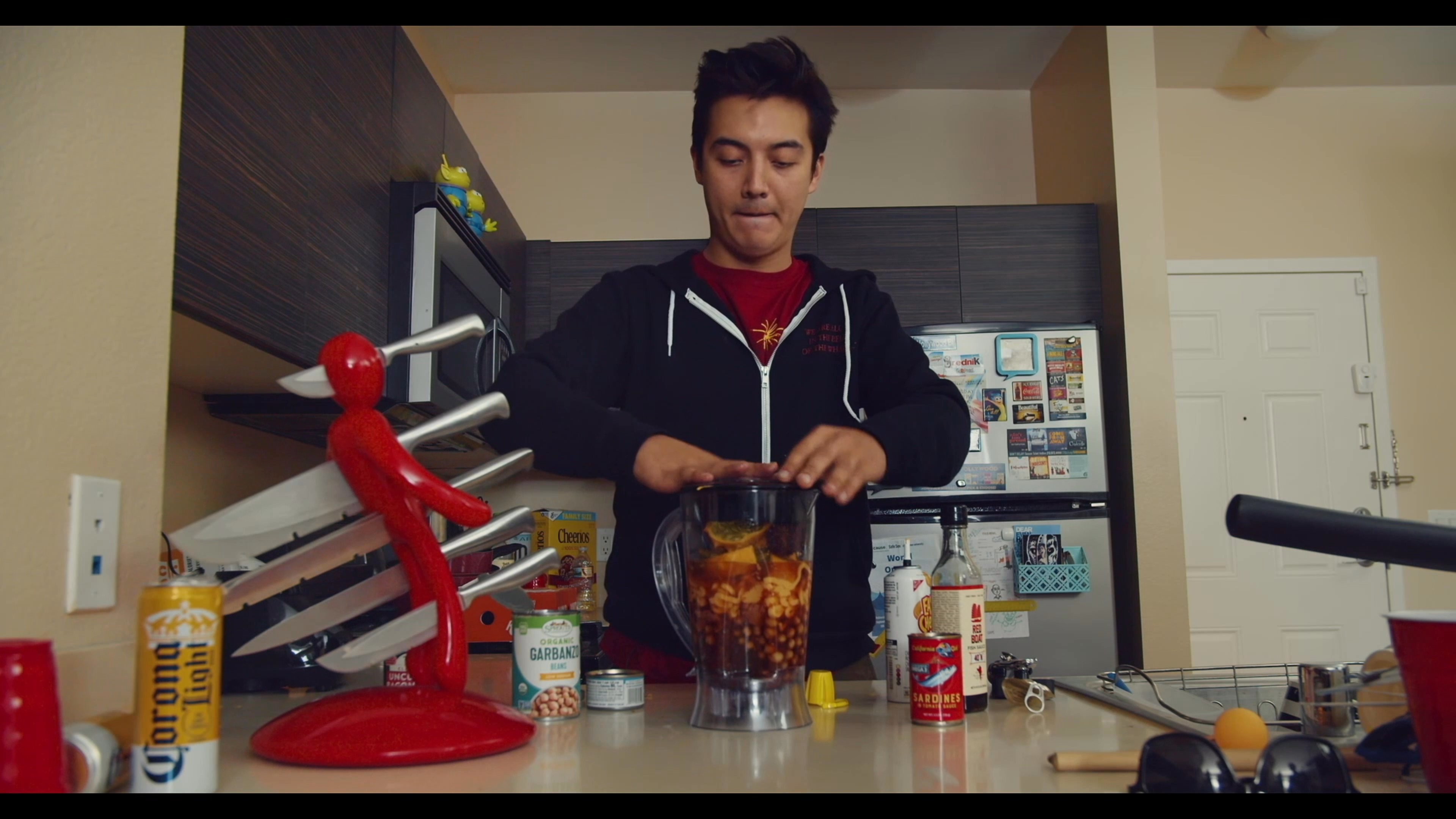 A man combines ingredients into a blender and activates the machine to process a beverage. Following the blending, he relaxes in the living room.