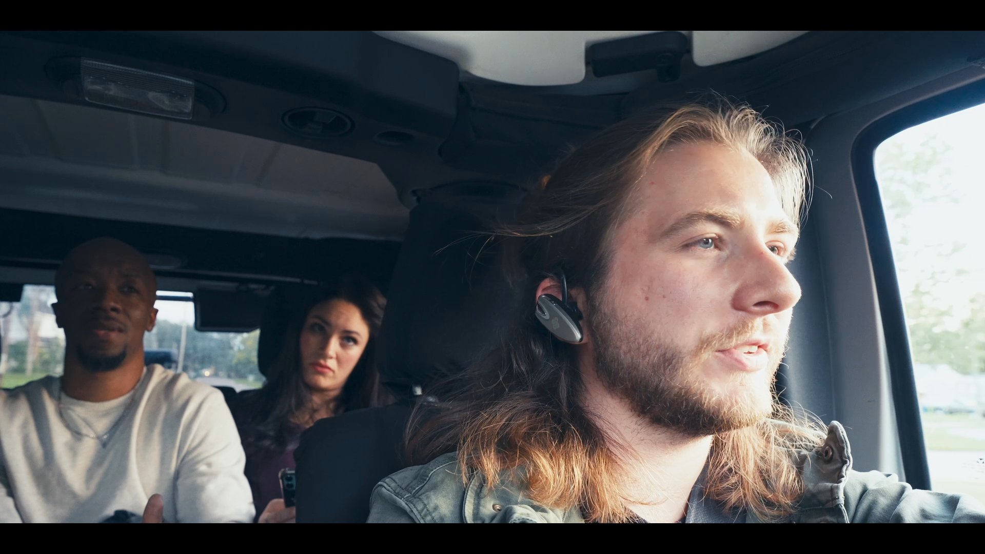 Two individuals engage in a serious discussion at an outdoor table, transitioning to a group travelling together in a vehicle.