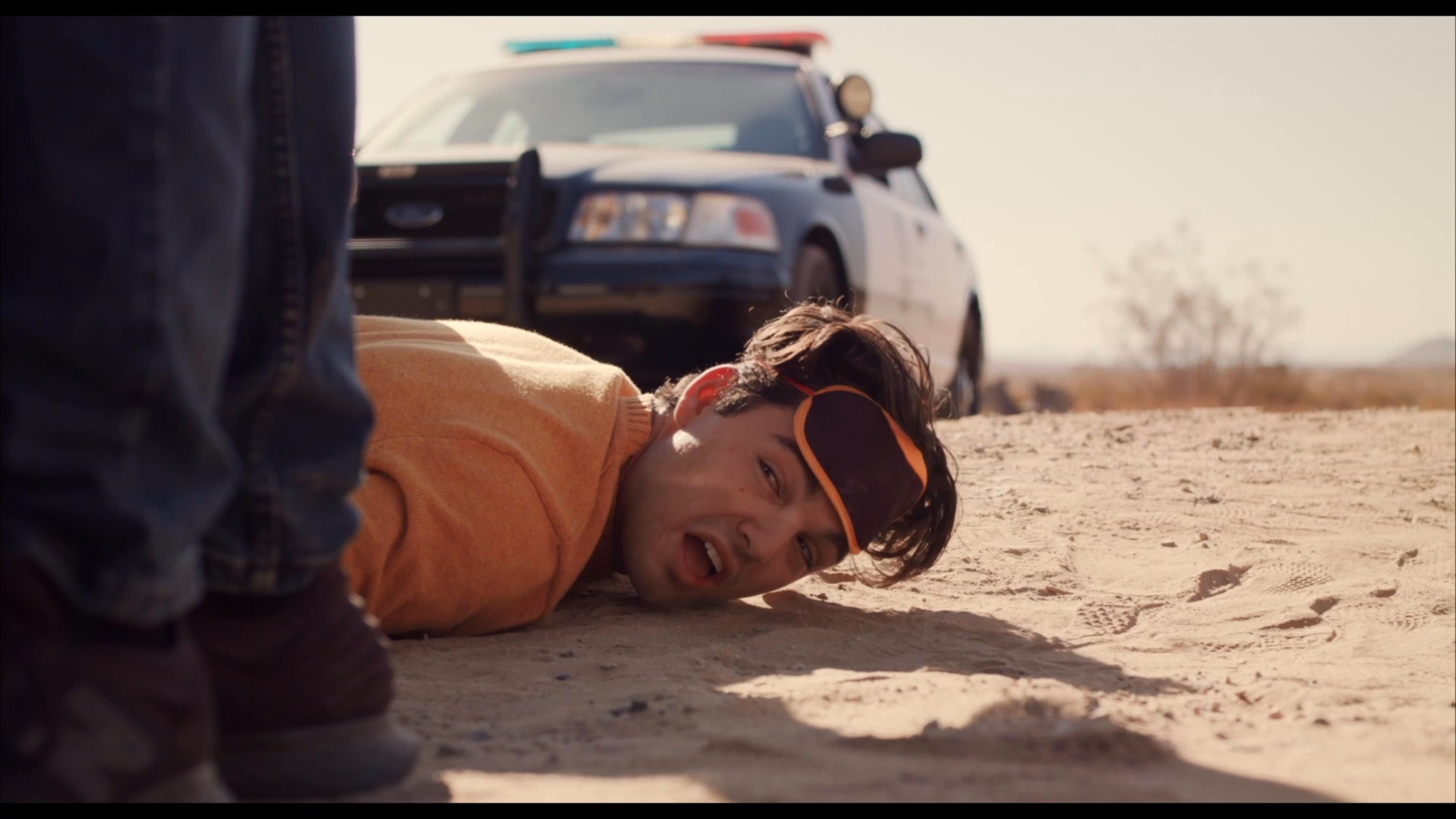Law enforcement officers detain a man in a desert environment while inspecting packages of Kinder Sorpresa candy found in a vehicle trunk.