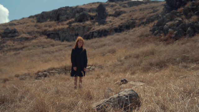 A man waking up in a field of dry grass with a girl in the background