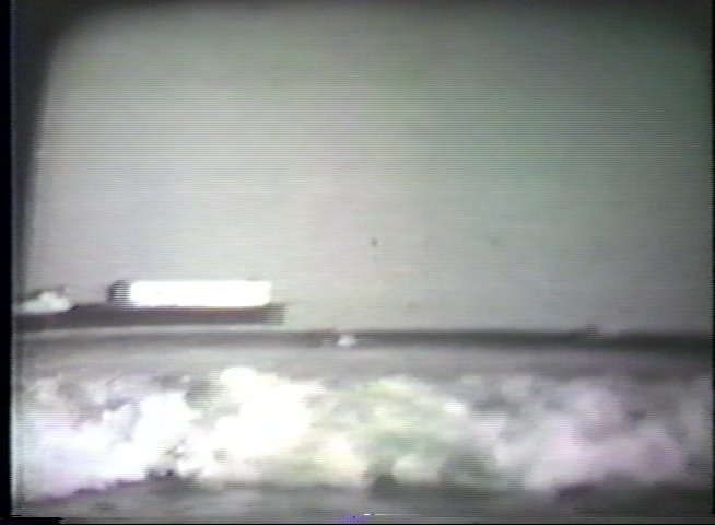 A surfer navigates waves near a coastal pier in this vintage, monochromatic sequence. The footage captures the movement of the ocean and the rhythmic motion of surfing.