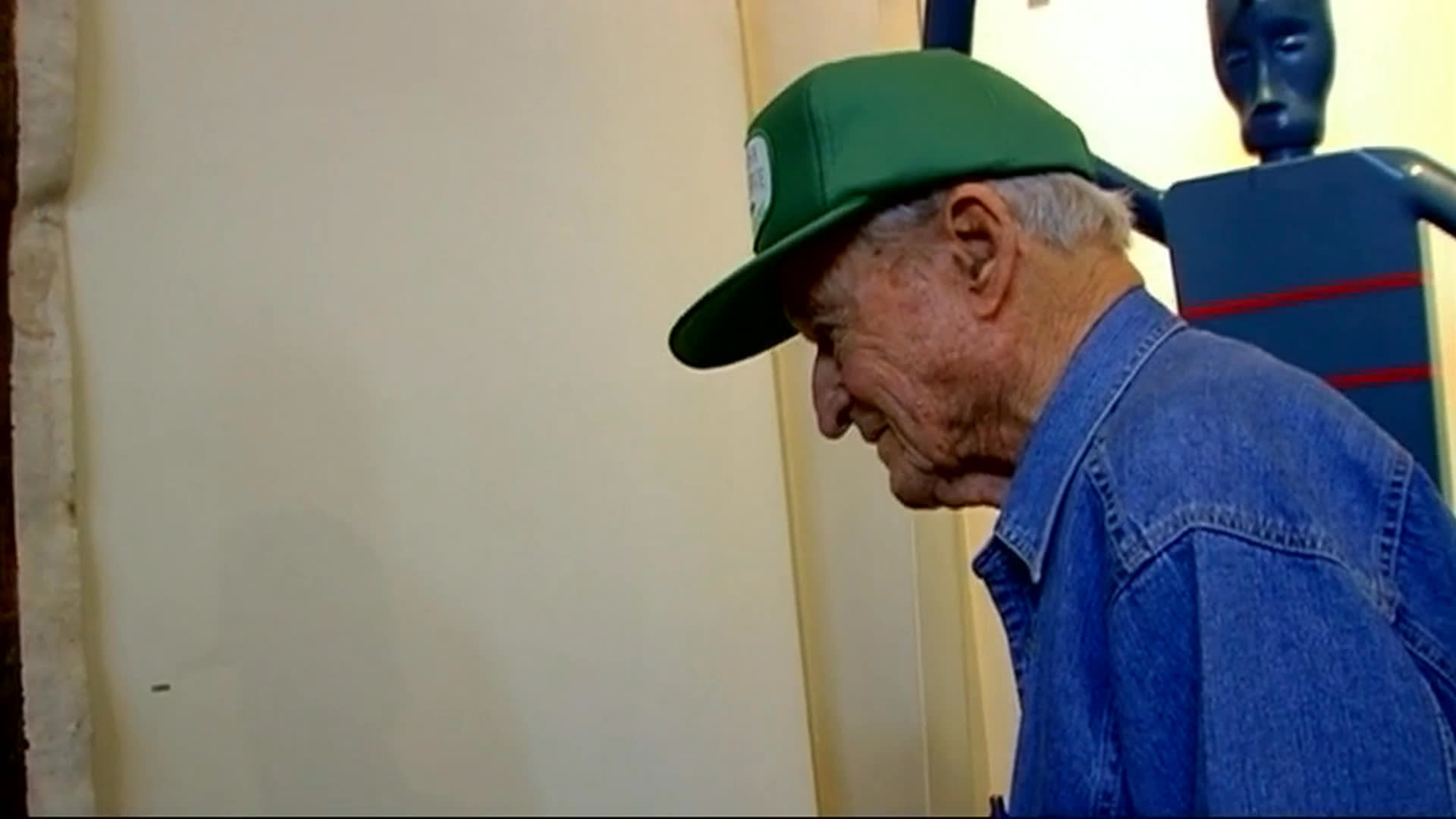 An elderly man in a green cap discusses his frustration with visitors focusing on museum labels instead of the artwork. Gallery visitors study paintings and distinctive exhibits as he argues that removing labels would encourage closer attention to the art.