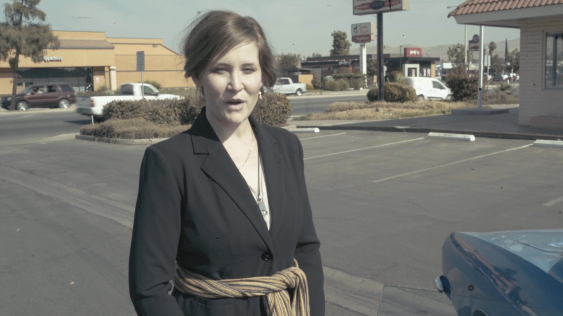 A man in a suit exits a diner and is confronted by a woman in a parking lot, leading to a violent altercation that leaves him critically wounded on the asphalt.