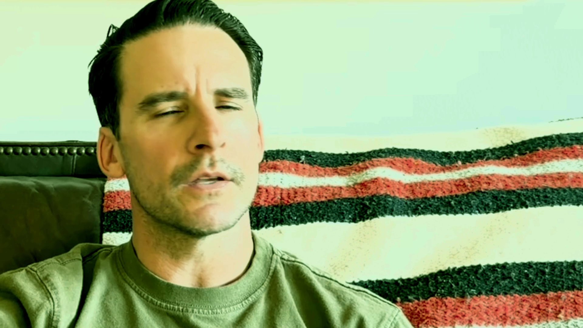 A man sits on a sofa, deeply lost in thought while observing his surroundings. His contemplative expression and subtle movements suggest a moment of quiet reflection.