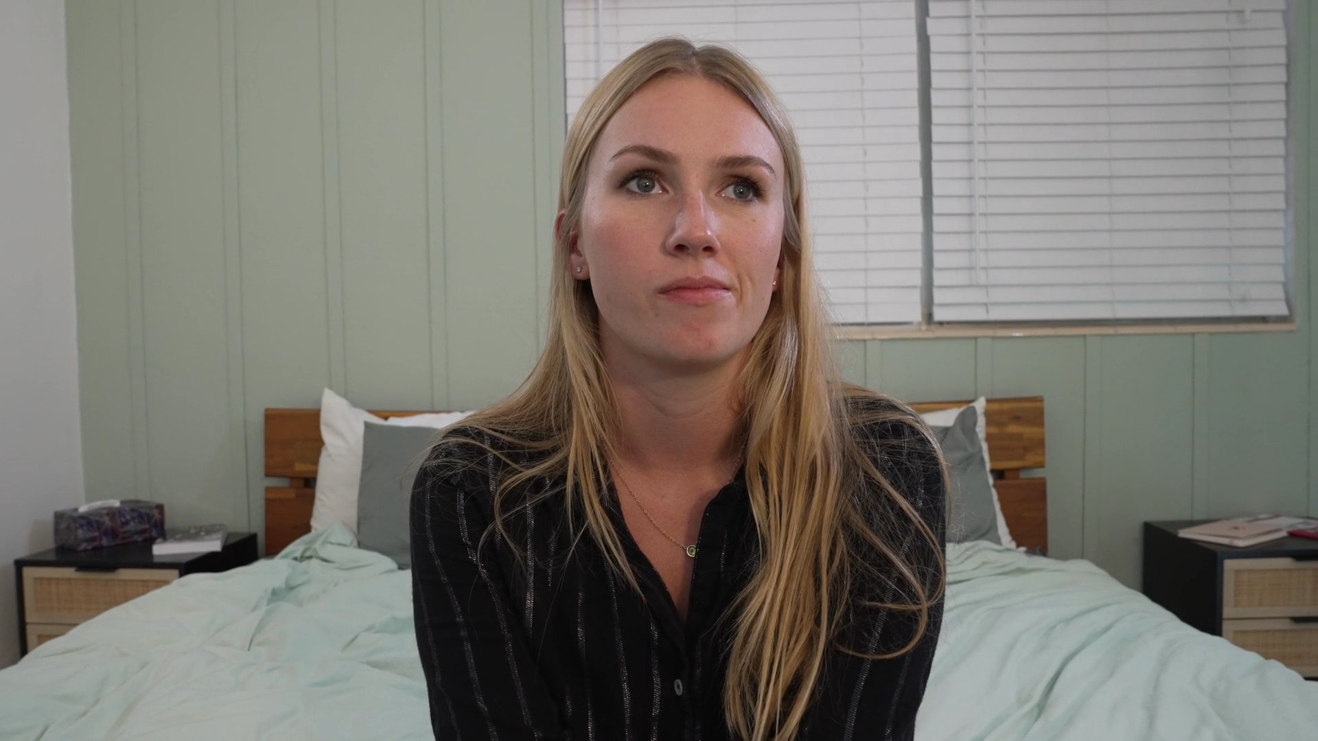 A woman delivers a direct-to-camera message from her bedroom, gesturing while sharing thoughts and personal insights.
