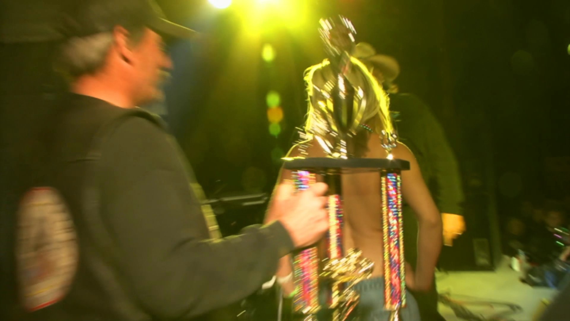 Participants dance on a stage at a crowded event before one is awarded a trophy.