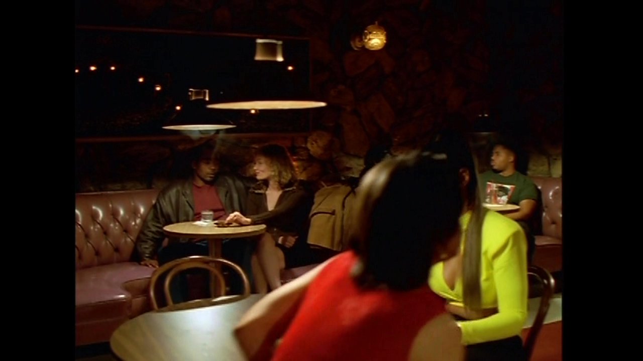 Patrons engage in quiet conversation while seated in booth tables within a dimly lit, atmospheric lounge environment.