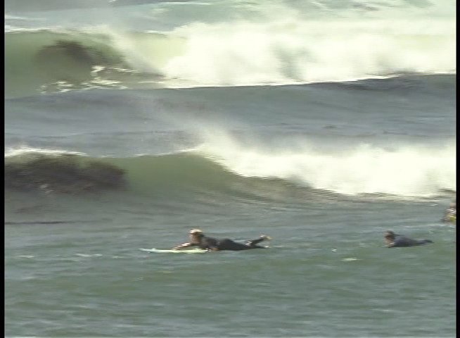 A seasoned surfer provides professional insights and commentary while intercut footage demonstrates surfers navigating ocean swells and breaking waves.