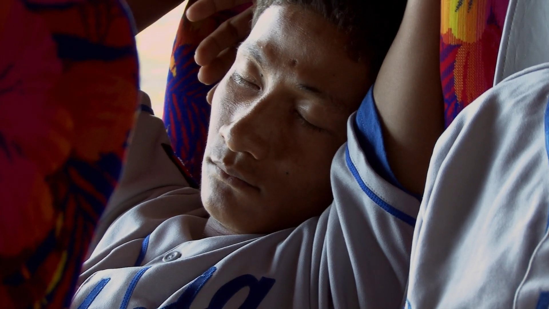 Baseball players in uniform rest and sleep on a bus during team travel.